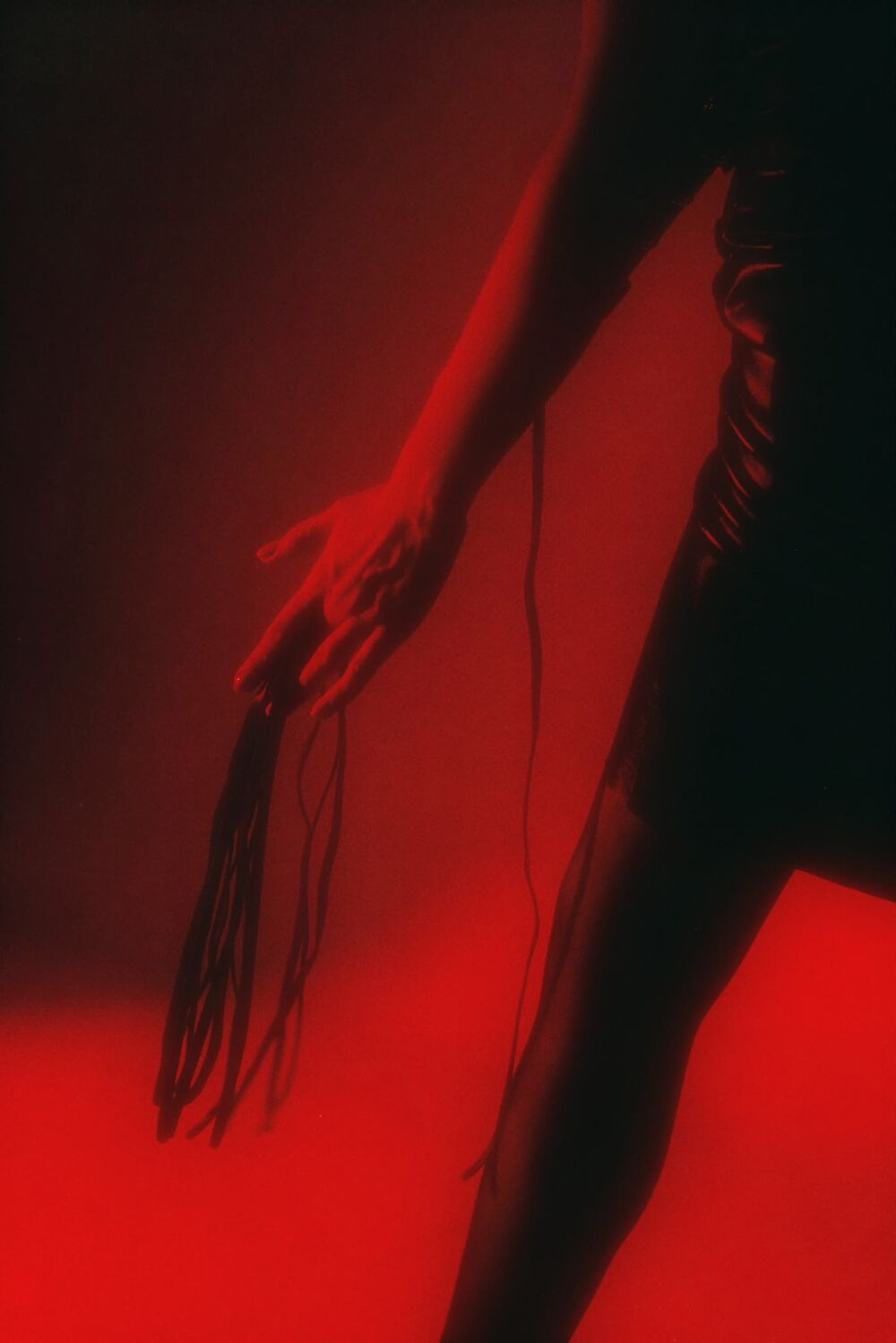 A hand lowering a flogger in red haze